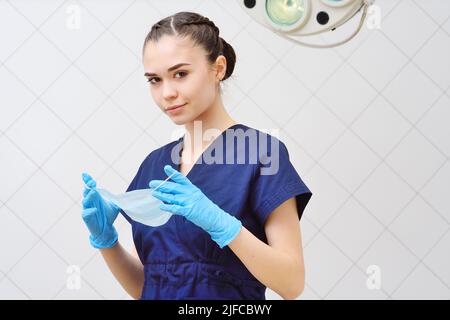 bella giovane donna in un vestito chirurgico mette su una maschera sterile. Foto Stock