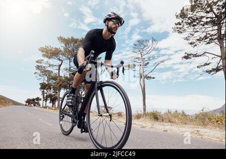 Un giovane atletico in bicicletta all'aperto. Sportivo uomo indossare casco e occhiali mentre si guida una bicicletta su una strada panoramica di montagna con il cielo in Foto Stock