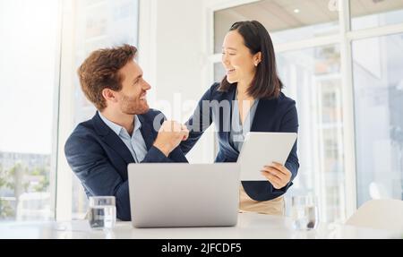 Due giovani e felici colleghi che lavorano insieme su un tablet digitale in ufficio. Fiduciosa donna d'affari asiatica e sorridente uomo d'affari caucasico Foto Stock