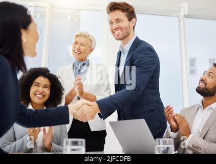 Sorridente giovane uomo d'affari che agita le mani con una donna d'affari durante una riunione in una sala d'ufficio. Diversi uomini d'affari che si acclamano e si aggrappano Foto Stock