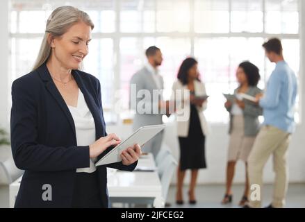 Matura felice donna d'affari caucasica che lavora su un tablet digitale in un ufficio. Un boss femminile sicuro sorridendo e tenendo un tablet digitale mentre si è in mano Foto Stock