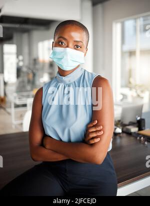 Giovane donna d'affari afroamericana in piedi con le braccia incrociate e con una maschera al lavoro. Un sicuro boss nero femmina indossando una maschera Foto Stock