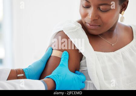Donna afroamericana che guarda il medico che applica un cerotto. Mano di un medico che applica un cerotto al braccio di un paziente. Paziente e medico in un Foto Stock