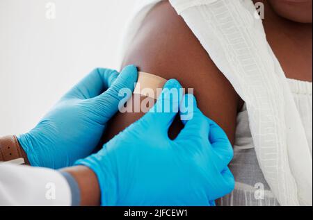 Mano di un medico che applica un cerotto ad un braccio del paziente. Primo piano di un medico che applica un cerotto su un paziente. Paziente afroamericano curato Foto Stock