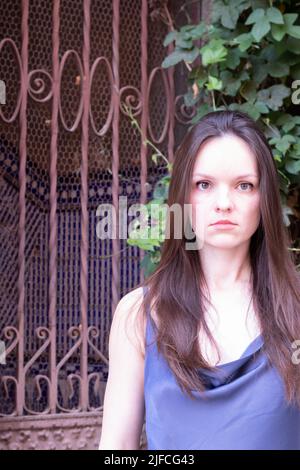 Ragazza in un abito in piedi con un cancello forgiato sullo sfondo Foto Stock