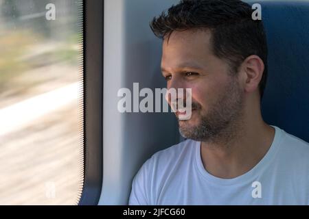 Ragazzo ispanico in treno sorridente e guardante fuori dalla finestra Foto Stock