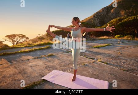 Donna yoga a tutta lunghezza che tiene la mano ai piedi posa in pratica all'aperto in natura remota. Bella persona caucasica usando il tappeto, bilanciamento mentre stretching Foto Stock