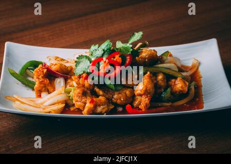 Primo piano di un piatto asiatico piccante con pollo e verdure in salsa al peperoncino su un piatto bianco Foto Stock