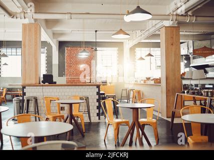 Interno di un moderno caffè vuoto o ristorante durante il giorno. Tavoli rotondi e sedie gialle in un caffè rustico. Caffetteria open space con tubi a vista Foto Stock