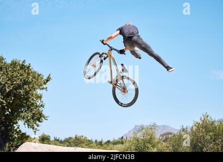 Uomo che mostra le sue abilità ciclistiche mentre fuori in bicicletta su una bicicletta fuori. Adrenalina junkie praticare un salto di sporcizia all'aperto. Maschio che indossa un casco fare Foto Stock