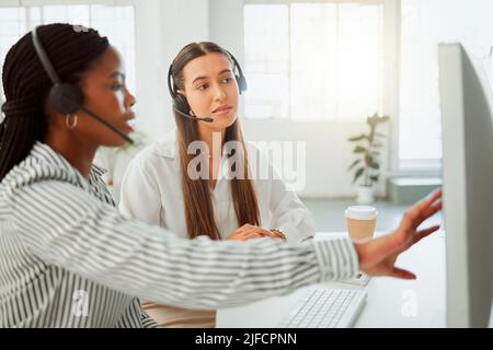 Giovane agente di telemarketing del call center ispanico che discute dei piani con un collega mentre lavora insieme su un computer in ufficio. Consulenti Foto Stock