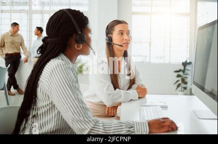 Giovane agente di telemarketing del call center ispanico che discute dei piani con un collega mentre lavora insieme su un computer in ufficio. Consulenti Foto Stock