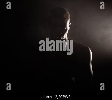 Un bel giovane afroamericano muscoloso in studio su sfondo scuro. Un atleta maschile macho che guarda pensieroso isolato su nero Foto Stock