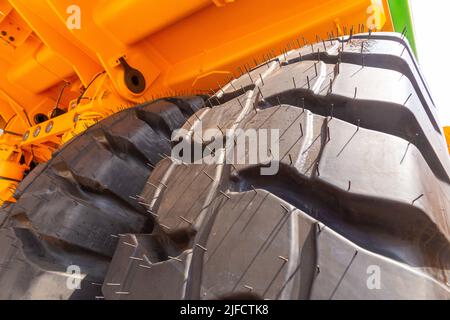 Enormi ruote posteriori del dumper a cassone ribaltabile con angolazione insolita in primo piano. Le ruote sono dotate di un battistrada per il movimento del dumper su terreni sfusi. Foto Stock