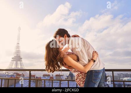 Non potete visitare Parigi e non innamorarvi. Scatto di una giovane coppia che condivide un momento romantico sul balcone di un appartamento con vista sulla Eiffel Foto Stock