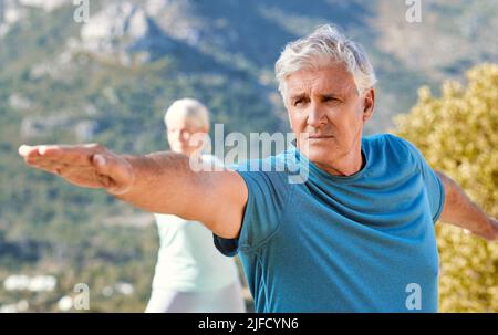 Anziani che vivono uno stile di vita sano ed esercitarsi all'aperto. Coppia anziana in piedi in posizione di guerriero mentre pratica yoga in natura in una giornata di sole Foto Stock