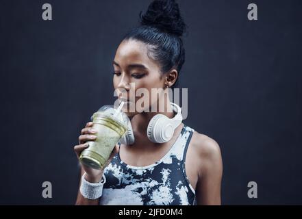 Una giovane donna da corsa attiva mista che beve un sano frullato disintossicante verde mentre si esercita all'aperto. Atleta femminile che sipping su frutta fresca nutriente Foto Stock