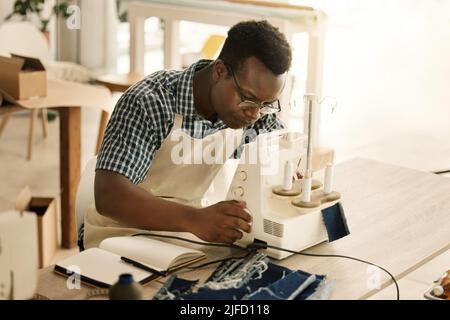 cucire un pezzo di denim afroamericano su misura. Giovane designer che usa la sua macchina da cucire. Cuciture su misura per un pezzo di tessuto. Messa a fuoco Foto Stock