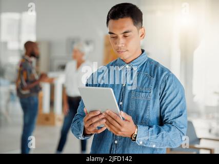 Un serio imprenditore asiatico che tiene e utilizza un tablet digitale al lavoro. Uomo d'affari cinese che lavora su un tablet digitale al lavoro. Affari Foto Stock