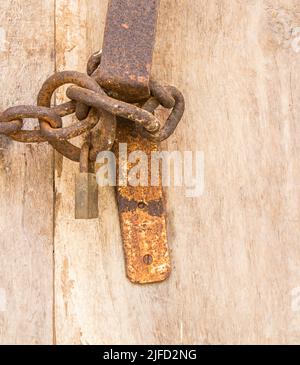 Vecchia catena di ferro arrugginita con lucchetto attaccato ad una porta di legno Foto Stock