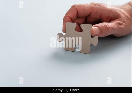 Mano maschio che tiene pezzo bianco puzzle in un'immagine concettuale di idea, strategia e soluzione. Su sfondo blu chiaro. Foto Stock