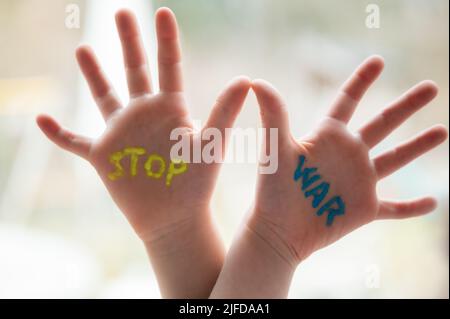 Stop war segno scritto sulle palme di un bambino in blu e giallo della bandiera ucraina. Foto Stock