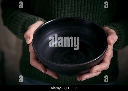 Alto angolo di raccolto anonima femminile in caldo maglione che tiene in mano elegante ciotola vuota in ceramica Foto Stock