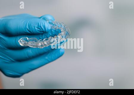 Mano dentista in guanti blu che presentano un allineatore trasparente rimovibile di fronte alla sala odontoiatria Foto Stock