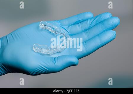 Mano dentista in guanti blu che presentano un allineatore trasparente rimovibile di fronte alla sala odontoiatria Foto Stock