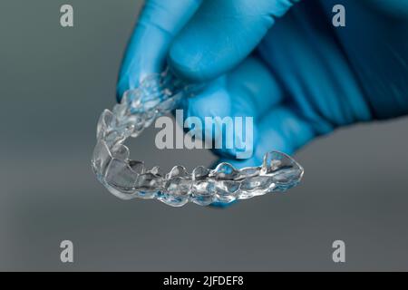 Mano dentista in guanti blu che presentano un allineatore trasparente rimovibile di fronte alla sala odontoiatria Foto Stock