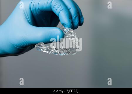 Mano dentista in guanti blu che presentano un allineatore trasparente rimovibile di fronte alla sala odontoiatria Foto Stock