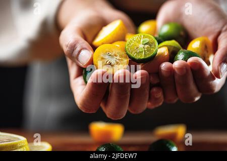 Tenendo molti piccoli kumquats e limes in entrambe le mani, il processo di fare una bevanda fredda fredda fredda fredda fredda fredda fredda e fruttata - foto di scorta Foto Stock