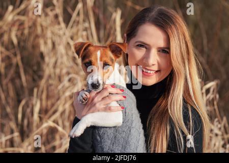 Giovane donna che tiene il suo cane terrier Jack Russell indossare abiti invernali caldi sulle mani Foto Stock