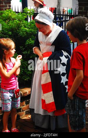 Un Reenactor di Betsy Ross dimostra che la bandiera fa in anticipo a due bambini ad una celebrazione americana del giorno della bandiera alla casa di Betsy Ross a Philadelphia Foto Stock