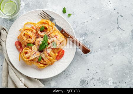 Gustosa e appetitosa classica tagliatelle italiana con salsa di pomodoro, parmigiano e basilico su piatto su tavolo leggero. Vista dall'alto, orizzontale Foto Stock