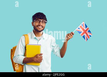 Ritratto di felice studente universitario indiano maschile con bandiera britannica su sfondo azzurro. Foto Stock