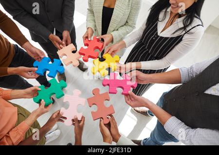 Immagine ritagliata di un gruppo di uomini e donne in piedi in cerchio e collegare pezzi di puzzle colorati. Foto Stock