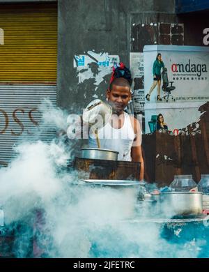 Kolkata, India - 26 Giugno, 2022: Un venditore di tè sulla strada che fa il tè al mattino presto con fumo in primo piano. Messa a fuoco selettiva. Foto Stock