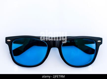 Elegante montatura nera in vetro solare realizzata in acetato con sfumature blu su sfondo bianco. Messa a fuoco selettiva. Foto Stock