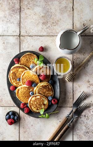 Pancake con lampone e mirtillo, congedo di menta, miele e posate rustiche su sfondo di piastrelle rosa, vista dall'alto Foto Stock