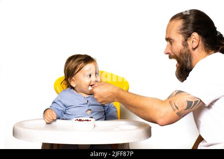 Papà ride e nutre il bambino sul seggiolone. Il concetto di passare il tempo con i bambini. Vista frontale foto su sfondo chiaro. Stile di vita Foto Stock