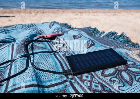 Pannello solare che carica un telefono cellulare su una spiaggia. Caricabatterie solare portatile powerbank alla luce del sole. Energia solare. Foto Stock
