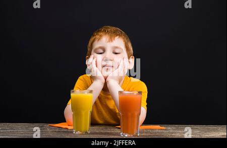 il ragazzo beve succo amaro e aspro dal pompelmo rosso, il succo non è delizioso e il bambino non piace, utile ma non delizioso grappa Foto Stock