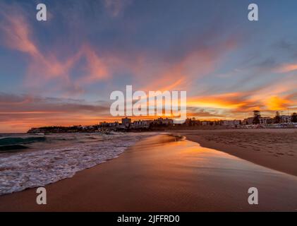 Splendidi cieli colorati mentre il sole sorge sulla famosa Bondi Beach a Sydney, Australia. Guardare a sud sulla sabbia deserta è magico Foto Stock