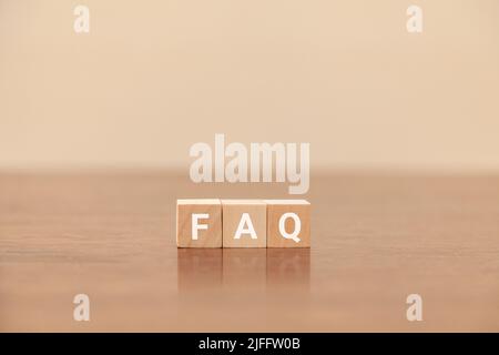 Testo delle domande frequenti. Domande frequenti. Domande frequenti. Scritto su tre blocchi di legno. Lettere bianche. Tavolo in legno e carta da parati bianca sul retro Foto Stock