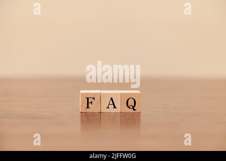 Testo delle domande frequenti. Domande frequenti. Domande frequenti. Scritto su tre blocchi di legno. Lettere nere. Tavolo in legno e carta da parati bianca sul retro Foto Stock