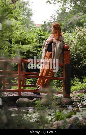 Felice zenzero capelli donna in ben curato parco o giardino. Libertà e stile di vita sano. Femmina nel suo 40s che riposa all'aperto. Allegro persona su Foto Stock