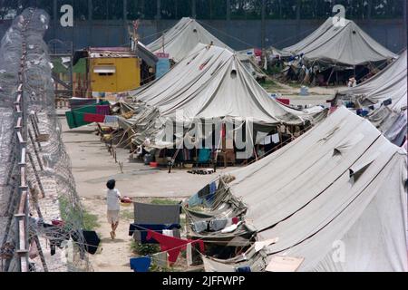 Centro di detenzione vietnamita di Shek Kong, eretto in poche settimane nel 1989 all'estremità occidentale della pista militare di Shek Kong, New Territories, Hong Kong. Le tende sono state erette sulla pista e l'erba su entrambi i lati, circondata da una recinzione in lamiera, sormontata da filo spinato. Decine di migliaia di richiedenti asilo vietnamiti sono passati attraverso il campo negli anni di attività. Foto scattata nel Dicembre 1990. Foto Stock