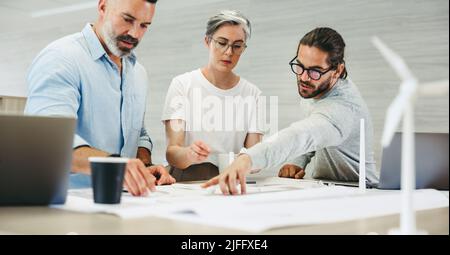 Gruppo di designer creativi che lavorano con progetti di turbine eoliche in un ufficio moderno. Team di uomini d'affari innovativi che si sfidano mentre si lavora su Foto Stock