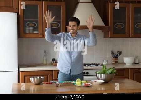 Il giovane bel latino si sposta alla musica che cucina in cucina Foto Stock